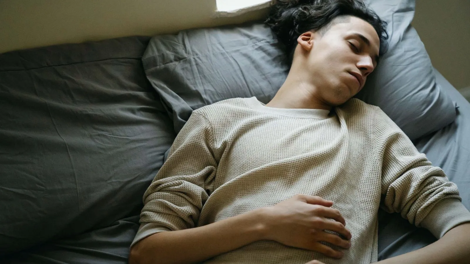 A young man asleep on his back in bed