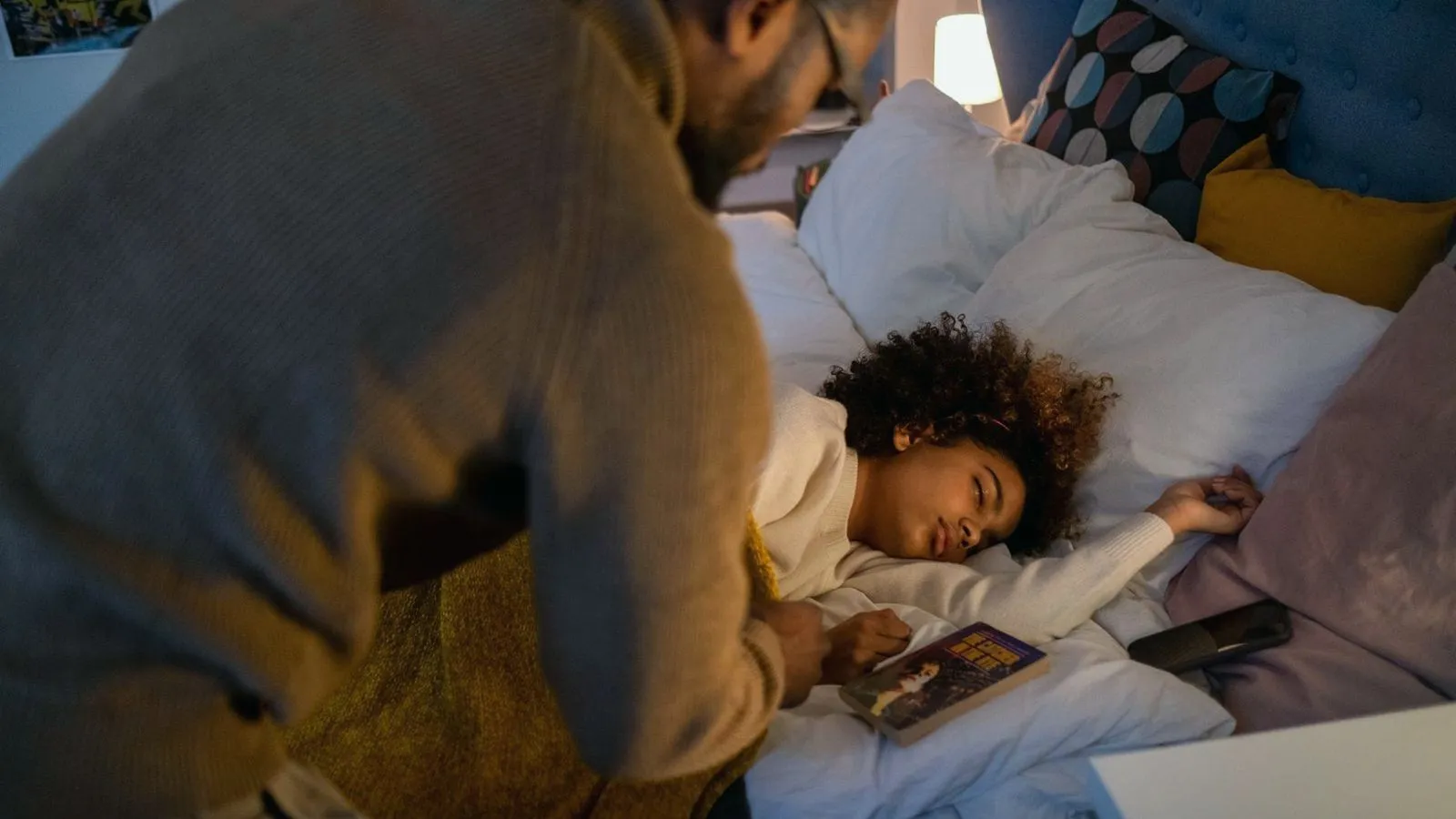 A parent settling a sleeping child into bed at night