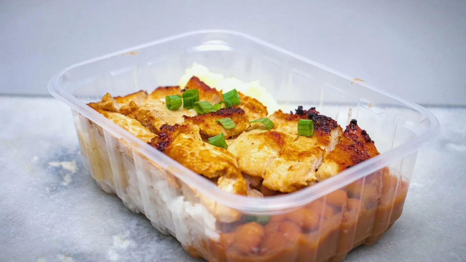 A cooked meal of chicken and vegetables in a clear container