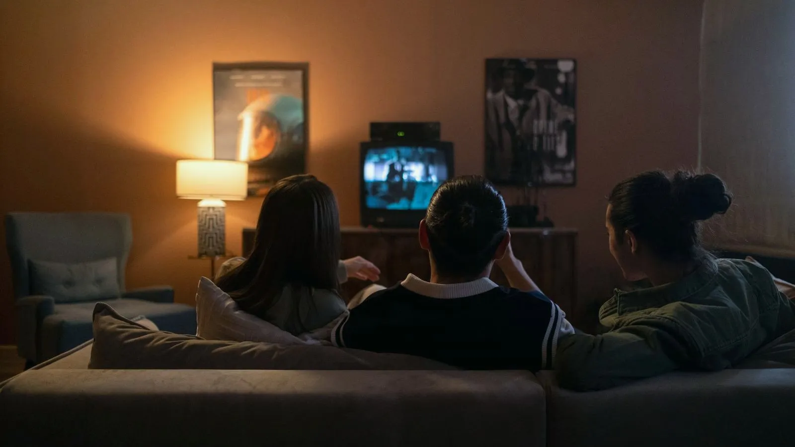 Three people sitting on a couch watching television in a dimly lit living room