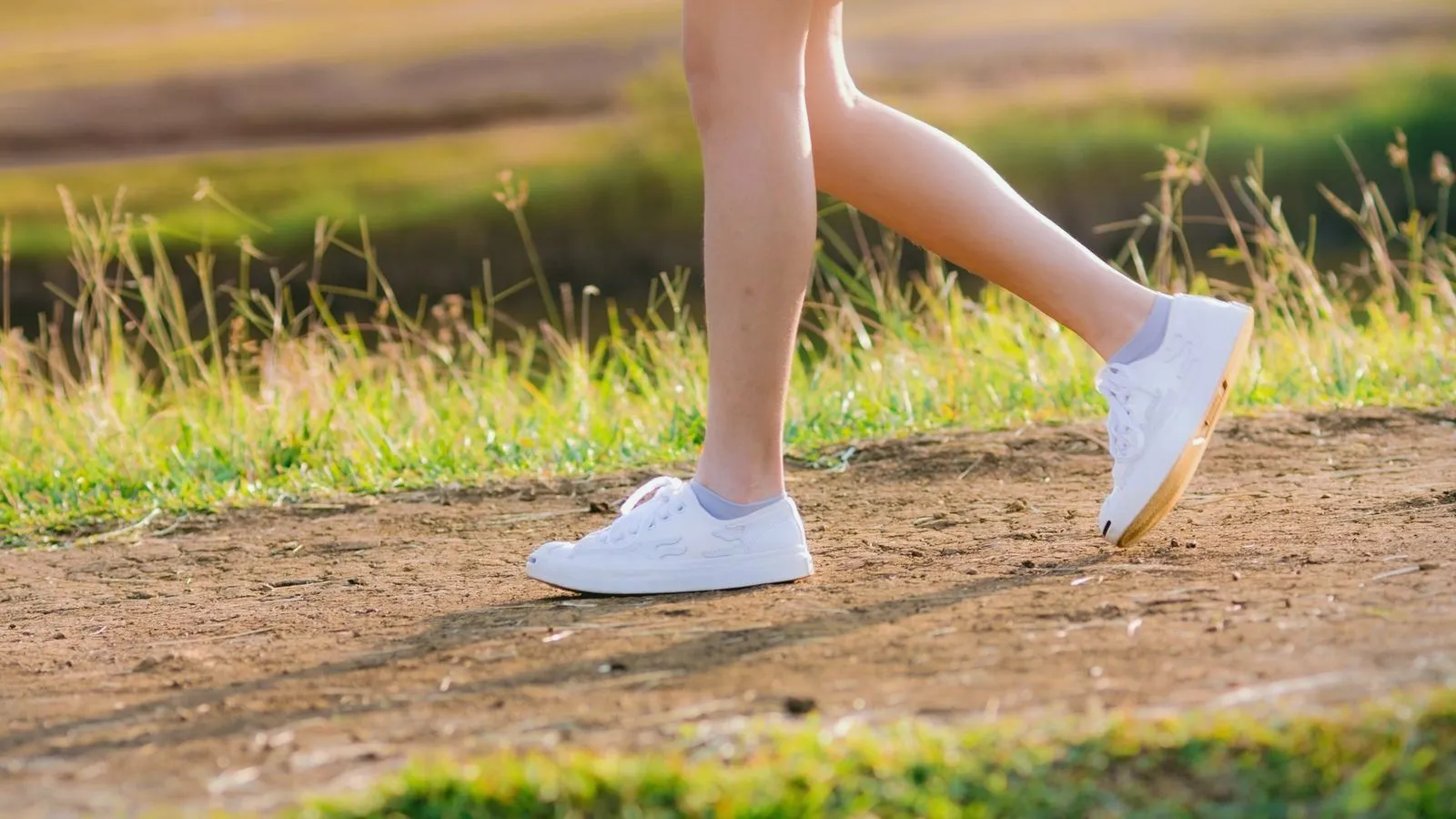 Legs mid-stride walking briskly along a sunlit dirt path