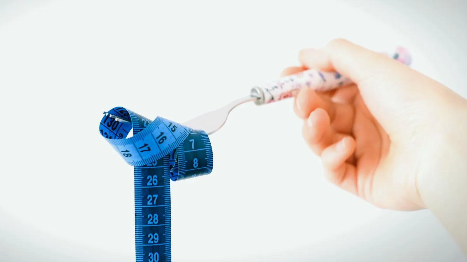 A fork wound with a blue measuring tape, held in one hand