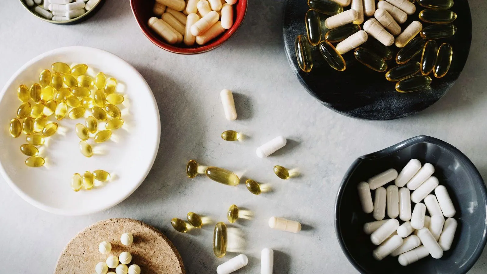 Assorted supplement capsules in small bowls on a pale surface